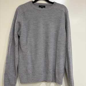 Grå stickad tröja från New Look - En stilren grå stickad tröja från New Look Men i storlek S. Tröjan har rund hals, diskret strukturmönster och långa ärmar. Perfekt för dig som gillar enkel och clean stil. Passar till jeans eller chinos för en chill look.