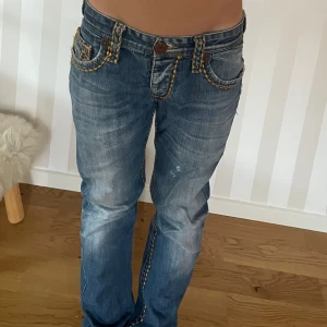 True Religion jeans  - Säljer ett par blå True Religion jeans med ikoniska kontrastsömmar i beige och orange. I fint skick! 