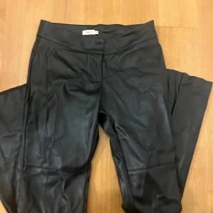 Svarta skinnbyxor från Nelly, stl 36 - Svart skinnbyxor från Nelly. Byxorna är utsvängda och low waist. Kommer aldrig till användning. 