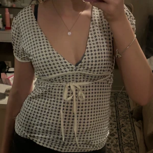 Vit blus med knyt från Vero Moda - Supersöt vit blus från Vero Moda med små mörkblå blommönster, v-ringning och korta puffärmar. Omlottkänsla med knytband under bysten som ger en snygg siluett. Perfekt till jeans eller kjol för en trendig look.