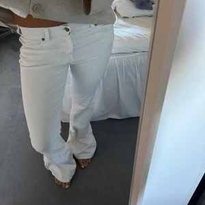Vita bootcut jeans med låg midja - Säljer ett par vita jeans med bootcut-modell och låg midja. Byxorna har klassisk femficksdesign och stängs med knapp och dragkedja. Snygg passform som sitter tajt upptill och släpper ut vid benen. Perfekta för en fräsch och trendig look.