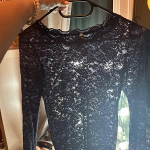 Mörkblå spetsblus från Rosemunde - Säljer en mörkblå långärmad spetsblus från Rosemunde. Blusen har vacker spets över hela plagget och en feminin, vågig kant vid halsringningen. Perfekt för dig som vill ha en elegant och stilren topp med transparent känsla.