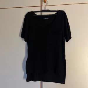 Svart t-shirt från Crocker XXS - En svart t-shirt från Crocker i storlek XXS. Modellen har rund halsringning, kort ärm och en bröstficka. T-shirten är rak i passformen och har slitsar i sidorna för en avslappnad look.