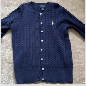 Marinblå kabelstickad kofta Polo Ralph Lauren - Snygg marinblå kofta från ralph lauren barn som är helt oanvänd och är i mycket bra skick! Om ni undrar något är de bara att skriva och pris kan diskuteras! Nypris cirka 1495!