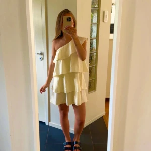 Ljusgul one shoulder volangklänning - Superfin ljusgul kortklänning med flera volanger och one shoulder-design. Klänningen har en luftig passform och är perfekt för varma dagar. 