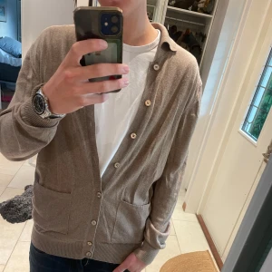 kofta från Stenströms - Säljer en klassisk beige kofta från Stenströms med knappar framtill och två fickor. Koftan har en mjuk känsla, ribbade muddar och krage. Perfekt att slänga över en t-shirt för en chill och stilren look.