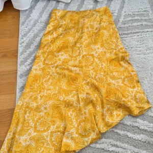 Gul paisleymönstrad långkjol Gina Tricot - Säljer en gul och vit långkjol från Gina Tricot med paisleyinspirerat mönster. Kjolen har en lätt A-linjeform och stängs med dragkedja i sidan. Perfekt för dig som gillar färgstarka och unika plagg.