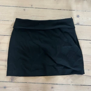 Svart kortkjol med dragkedja - Enkel svart kortkjol med bred linning och diskret dragkedja i sidan. Kjolen har en rak passform och är tillverkad i ett mjukt tyg som känns bekvämt. Perfekt att styla med en crop top eller oversized tröja.