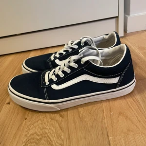Vans Old Skool sneakers - Klassiska Vans Old Skool sneakers i storlek 39, i mörkblå canvas med vit sula och vit sidostrip. Skorna har snörning och den ikoniska röda 'Off The Wall'-loggan bak. Perfekta för dig som gillar streetstyle och skatekänsla.