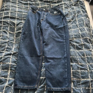 Blå wide jeans från Lorenzo, stl 32 - Säljer ett par blå jeans från Lorenzo i storlek 32. Modellen har breda ben och klassisk femficksdesign. På bakfickan finns en stor vit stjärna med broderad logga. Jeansen har normal passform och är tillverkade i robust denim.
