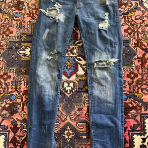 Dsquared2 - Säljer ett par blå jeans från Dsquared2 med  slitningar och trasiga detaljer framtill. Slim fit med klassisk femficksdesign och läderpatch bak i midjan. Skick 9/10, knappast använd. Om du har fler frågor eller är intresserad. Skriv privat 
