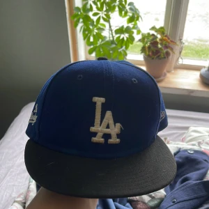 Blå LA Dodgers keps från New Era - Säljer en klassisk blå LA Dodgers keps från New Era med svart skärm och broderad LA-logga framtill. Sidan har Los Dodgers-broderi och baksidan har MLB-logga. Perfekt för dig som gillar sportig streetstyle.