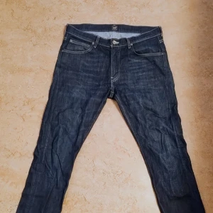 Mörkblå jeans från Lee - Snygga mörkblå jeans från Lee med klassisk femficksdesign och kontrastsömmar. Jeansen har rak passform och är tillverkade i slitstarkt denimtyg. Perfekta för dig som gillar en tidlös och clean look.