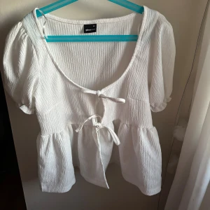 Vit blus med knyt från Gina Tricot - Supersöt vit blus från Gina Tricot i storlek XS. Den har puffiga korta ärmar, volang nertill och två knyt framtill. Materialet är strukturerat och lätt, perfekt för en fräsch look. Använd få gånger och inga defekter! Läs gärna bio och ställ gärna frågor🩷