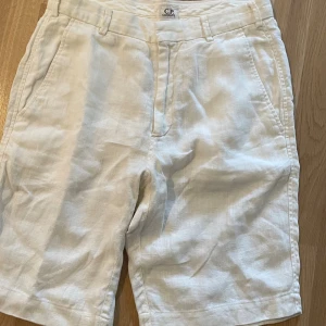 Vita linneshorts från C.P. Company - Snygga vita shorts från C.P. Company i luftigt linne. Klassisk design med fickor på sidorna och hällor för bälte. Perfekta för varma dagar när du vill ha en clean och stilren look.