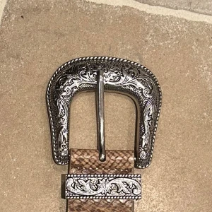 Snakeprint bälte - Snyggt brunt bälte med ormmönstrad yta och detaljerad silverspänne med graverade blommor. Bältet har western-vibe och passar perfekt till jeans. Spännet och hållaren har fina mönster som sticker ut.