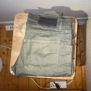 Olivgröna jeansbyxor med raka ben från Tiger of Sweden - Snygga olivgröna jeansbyxor med klassisk femficksdesign och svart läderpatch i midjan. Byxorna har raka ben och är tillverkade i ett slitstarkt bomullsmaterial som ger en skön känsla. Perfekt för dig som gillar en enkel och stilren look.