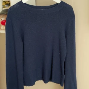 Mörkblå stickad tröja från H&M - En enkel och stilren mörkblå stickad tröja från H&M. Tröjan har rund halsringning, långa ärmar och ribbade muddar vid ärmslut och nederkant.