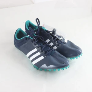 Adidas Adizero blå löparskor  - Snygga Adidas Adizero löparspikskor i marinblått med vita ränder och turkosa detaljer. Skorna har snörning, spetsig tå och metallspikar under sulan för max grepp på banan. Ovandelen är i syntetmaterial och insidan har en turkos vaddering för extra komfort. stl. 46 2/3 (UK 11.5)