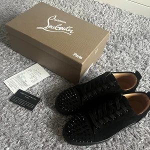 Svarta Louboutin skor - Säljer ett par svarta sneakers från Christian Louboutin med ikonisk röd sula och svarta nitar på tån. Skorna har snörning och är tillverkade i mocka och skinn, vilket ger en lyxig känsla. De är storlek 41 och tillkommer med Box, kvitto och kort, tveka inte att höra av dig. Byten funkar. De är bara använda en gång och ifall du önskar att se fler bilder fråga gärna. Den här är fri frakt versionen av den andra satt det blir billigare