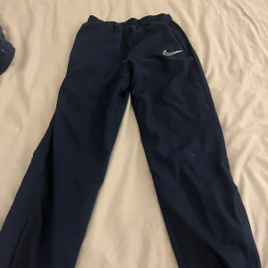 Nike Dri-Fit mörkblå träningsbyxor L -  2. ST Mörkblå träningsbyxor från Nike med Dri-Fit-teknologi. Byxorna har elastisk midja och en enkel, sportig look med Nike-logga på låret. Perfekta för dig som gillar att röra på dig och vill ha bekväma byxor i funktionsmaterial.