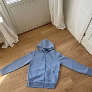 Ljusblå hoodie från Polo Ralph Lauren - Ljusblå zip hoodie från Polo Ralph Lauren. Storlek M, ny med taggar endast provad.