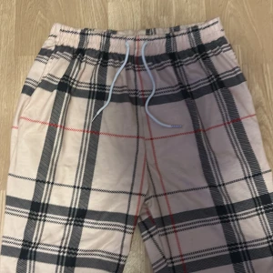 Beigea burberry shorts  - Snygga beige shorts med klassiskt rutigt mönster i svart och rött. De har elastisk midja med vit snörning för skön passform. Perfekta för chill dagar och har en loose fit som ger en avslappnad vibe. Materialet känns lätt och bekvämt mot huden.
