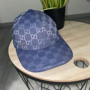 Blå keps från Gucci i jeans - Snygg blå keps från Gucci i jeansmaterial med klassiskt GG-mönster över hela kepsen. Justerbar rem baktill och vit insida med märkets etikett. Perfekt accessoar för att lyfta din streetstyle o ingen box elr kvitto tyvärr men även öppen för byten helst