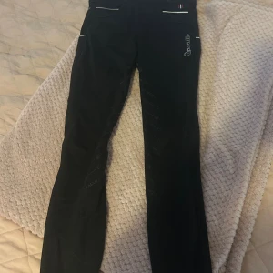 Svarta ridbyxor från Cavallo - Svarta ridbyxor från Cavallo med silikongrepp och fleecefodrad insida. Byxorna har vita detaljer vid fickorna och logga på låret. Perfekta för kalla dagar i stallet och har en tight passform som ger bra rörelsefrihet.