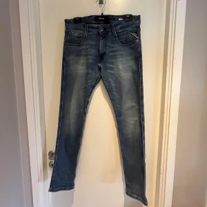 Replay Anbass blå jeans, storlek 30 - Snygga Replay Anbass jeans i blå tvätt med slitningar och klassiska detaljer. Modellen har fem fickor, smal passform och tydliga sömmar på bakfickorna. Perfekta för dig som gillar en modern och stilren look. Byxorna är i bra skick! Priset går att diskutera💸