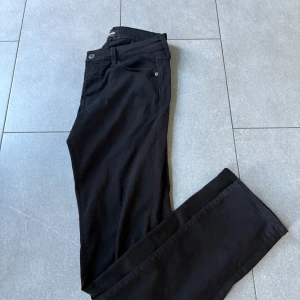 Svarta slim jeans från Jack & Jones - Svarta jeans från Jack & Jones i modellen Slim Glenn. Snygg, smal passform med klassiska fem fickor och bälteshällor. Materialet är mjukt och stretchigt för extra komfort. Perfekt för dig som gillar en stilren och enkel look.