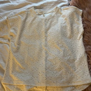 Vit broderad blus från ONLY - Säljer en vit blus från ONLY i storlek M. Toppen har ett broderat hålmönster över hela tyget och är ärmlös med rund halsringning. Perfekt för dig som gillar romantiska detaljer och en luftig känsla. Använd en gång. Den har en fläck på ryggen. 