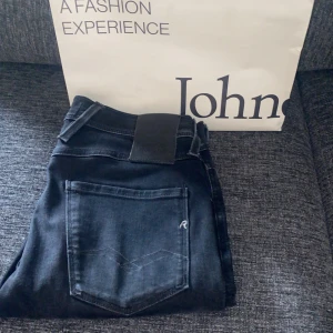 Replay Anbass svarta jeans - Snygga Replay Anbass jeans i svart tvätt med klassisk femficksdesign och diskret Replay-logga på fickan. Slimmad passform och stretchigt jeanstyg som sitter skönt hela dagen. Perfekt för dig som gillar stilrena och moderna jeans.