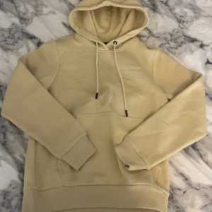 Beige hoodie Peak Performance XS - Säljer en hoodie från Peak Performance i storlek XS. Tröjan har huva med snörning, broderad logga på bröstet och en klassisk känguruficka framtill. Mjuk bomullskänsla och ribbade muddar vid ärmslut och nederkant. Helt oanvänd och lappen kvar original pris 1300