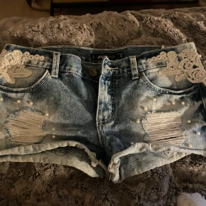 Lågmidjade coola jeansshorts! - Säljer nu ett par asss coola jeansshorts med slitningar,pärlor och vita detaljer! Älskar de men andvöndet de inte så säljer!!🥰Stolrke S!!Pris kan diskuteras 