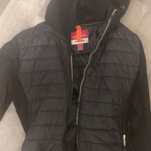 Svart pufferjacka Parajumpers L - Säljer en svart pufferjacka från Parajumpers med huva och dragkedja framtill. Jackan har quiltad framsida, släta ärmar och snyggt PJS-märke på ena ärmen. Perfekt för dig som vill ha en stilren och sportig look.