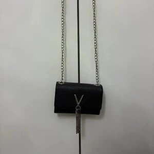 Svart axelväska från Valentino - Snygg svart axelväska från Valentino med silverfärgad kedja och V-logga framtill. Väskan har en stilren rektangulär form och är tillverkad i skinn med en elegant struktur. Framtill hänger dekorativa silverkedjor under loggan för extra detalj.