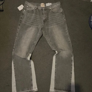 Grå jeans från Gallery Dept. - Snygga grå jeans från Gallery Dept. passar M-L. Och s om man vill ha de baggy. med ljusare paneler längs sidorna och råa kanter vid bensluten. Modellen har klassisk femficksdesign och raka ben med en loose passform. Perfekt för dig som gillar streetwear och unik stil.