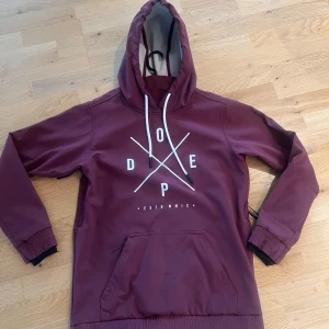 Vinröd skidjacka från Dope XS - Säljer en vinröd skidjacka/skidhoodie från Dope i storlek XS. Tröjan har stor huva med snörning, magficka och tryck på bröstet. Utsidan är slät och insidan är fodrad med mjuk fleece. Perfekt för kyliga dagar! Som man ser på bilderna har den tydliga slitningar, därav priset. Skriv för fler detaljerade bilder. 🥰🤗