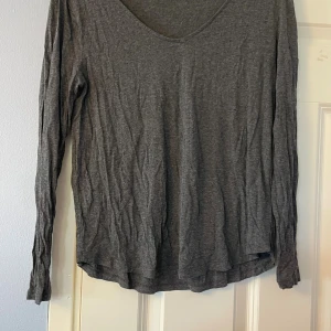 Mörkgrå basic långärmad tröja S - En enkel och mjuk mörkgrå långärmad tröja från Basic i storlek S. Tröjan har rundad halsringning och är tillverkad i ett tunt och skönt bomullsmaterial. Perfekt att ha som lager eller till chill dagar.