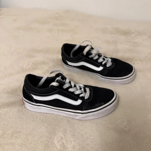 Svarta sneakers - Svarta Vans Old Skool sneakers med vit sula och klassisk vit sidostripes. Skorna har snörning med vita skosnören och rund tå. Ovandelen är i mocka och canvas, med Vans-logga på hälen. Varan kommar skickas rena.