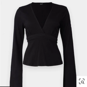 Svart omlottopp med knyt i ryggen - Snygg svart omlottopp från Gina tricot med v-ringning och långa ärmar. Toppen har ett knytband i ryggen som ger en extra detalj och markerar midjan. Storleken är L.