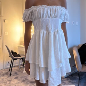 Vit omlottklänning med volanger - Supersöt vit kortklänning med omlottvolanger och puffiga offshoulder-ärmar. Klänningen har ett lätt strukturerat tyg med små broderade detaljer och smock i ryggen för skön passform. Perfekt för sommarens alla tillfällen och ger en romantisk vibe PERFEKT OM DU SKA VARA PIRAT