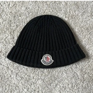 Moncler mössa - Svart ribbstickad mössa från Moncler. I mycket bra skick men däremot saknas lapp i mössan pga de kliade.