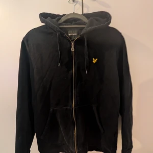 Svart hoodie från Lyle & Scott - Svart hoodie från Lyle & Scott med dragkedja, huva och snörning. Klassisk gul logga på bröstet och två fickor framtill. Perfekt för chill dagar eller när du vill ha en enkel och stilren look. Skriv för frågor och bilder (: ⚠️ÄKTA⚠️
