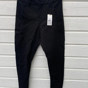 Nya svarta tapered byxor från Kappahl - Svarta byxor från Kappahl i storlek 38 med prislappen kvar. Smalare passform och normal midja. Byxorna har fickor fram och fuskfickor bak, bälteshällor och är gjorda i ett mjukt material med lite stretch. Snygg, enkel och stilren design som funkar till många stilar. Tyvärr fel storlek för mig. 