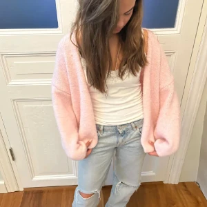 Ljusrosa stickad kofta - Supermjuk och fluffig ljusrosa kofta från Lindex. Koftan har en oversized passform med breda ärmar och öppen front utan knappar. Tröjan är aldrig använd och har prislappen kvar. 