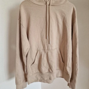 Beige hoodie med ficka och huva - Säljer en beige hoodie med klassisk känguruficka och dragsko i huvan. Tröjan har en relaxed passform och är tillverkad i mjuk bomullsmix, perfekt för chill dagar. Långa ärmar och ribbade muddar ger en skön vibe.