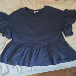 Mörkblå volangblus från Kappahl - Supersöt mörkblå blus från Kappahl med volangärmar och volang nertill. Blusen har rund halsringning och är tillverkad i mjuk bomull. Perfekt för dig som gillar en trendig och lekfull stil med extra volym på ärmarna. Ny och alldrig använd därefter priset ❤️