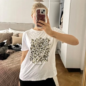 Vit t-shirt med leopardmönster - Säljer en vit t-shirt med coolt leopardmönster framtill. T-shirten har korta ärmar och en klassisk rund hals. Perfekt för dig som gillar djurmönster och vill ha en chill och trendig look.
